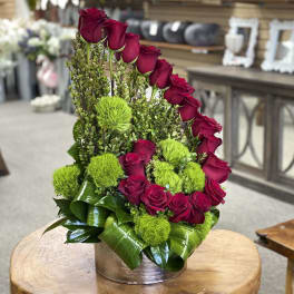 Red roses arranged with bright green pom-pom flowers in a round vase