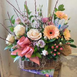 Basket arrangement of peach roses, gerbera daisies, and pink ribbon