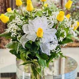Yellow roses arranged in a clear glass vase with white ribbon