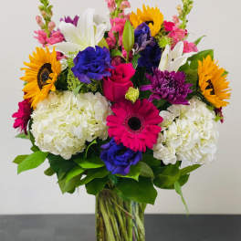 Colorful mixed bouquet in a clear glass vase with sunflowers, lilies, and hydrangeas