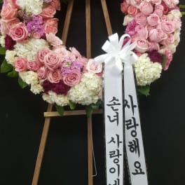 Pink and white floral wreath on a wooden stand with ribbon streamers