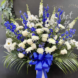 Large white and blue floral spray in a white vase with a blue ribbon