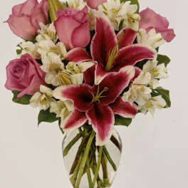 Clear glass vase with pink roses, pink lilies, and white alstroemeria in a mixed bouquet