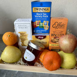 Gift basket with fruit, tea, biscuits, and honey in a wooden tray