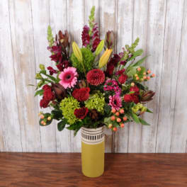 Tall mixed bouquet in a yellow vase with red, pink, and green blooms