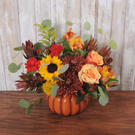 Autumn floral arrangement in an orange pumpkin vase with sunflowers and roses