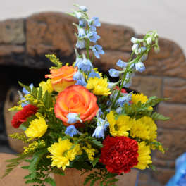 Colorful flower arrangement in a wooden cube vase with roses, daisies, and blue delphinium