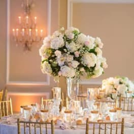 Tall white floral centerpiece in a clear vase on a banquet table