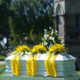 White casket with yellow floral sprays and draped yellow fabric outdoors