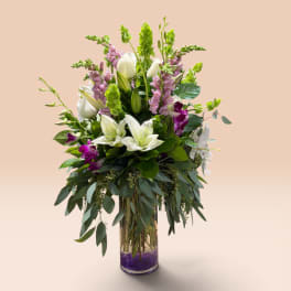 Tall bouquet of white lilies and purple flowers in a glass vase