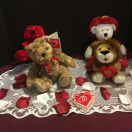 Three plush teddy bears with heart-themed accents on a lace cloth