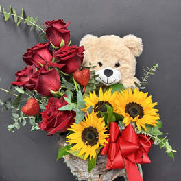 Red roses and sunflowers with a teddy bear and red ribbon in a rustic container