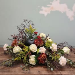 Low floral centerpiece with white roses, red mums, and a black pumpkin