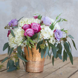 Bouquet of pink roses, white hydrangeas, and lavender blooms in a copper vase