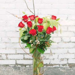 Red roses arranged in a tall glass vase with branches and greenery
