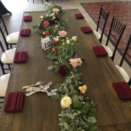 Long floral garland centerpiece on a dining table with small glass vases