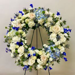 Large floral wreath with white roses and blue flowers on a stand