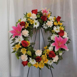 Circular floral wreath with red roses, pink lilies, and white daisies
