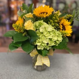 Bouquet of sunflowers, pale green hydrangea, and yellow roses in a glass vase