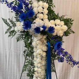 Standing floral spray with white flowers, blue accents, and a ribbon on an easel