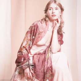 Woman wearing a pink floral shawl and pale dress against a soft pink backdrop