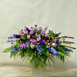 Large purple and blue floral arrangement in a white pedestal vase