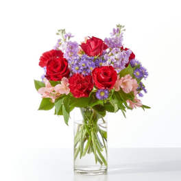 Red roses and purple flowers arranged in a clear glass vase
