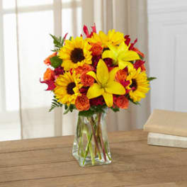 Bouquet of yellow sunflowers and orange roses in a clear glass vase