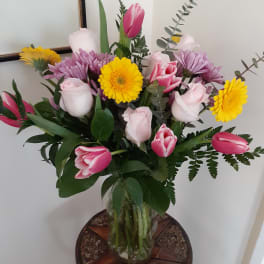 Mixed bouquet of pink tulips, pale roses, and yellow daisies in a glass vase