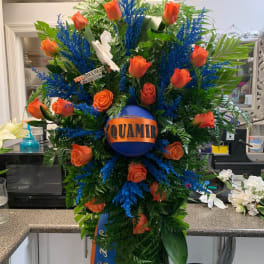 Large orange rose funeral spray with blue accents and a memorial ribbon
