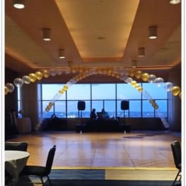 Balloon arch in gold, white, and clear balloons inside a banquet room