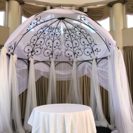 White draped wedding canopy with black scrollwork and a round table beneath