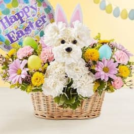 Basket arrangement with a white plush dog, pastel flowers, and a Happy Easter balloon