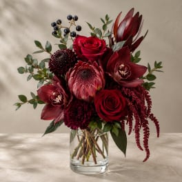 Deep red bouquet in a clear glass vase with roses and tropical blooms
