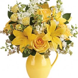Yellow roses and lilies arranged in a yellow pitcher vase
