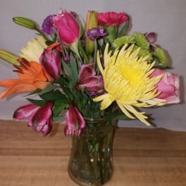 Mixed bouquet of pink, yellow, orange, and purple flowers in a glass vase