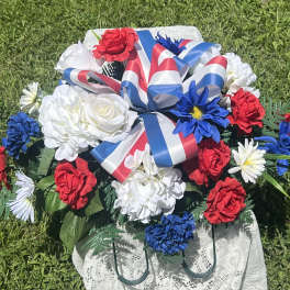 Red, white, and blue floral arrangement with ribbon on a lace-covered stand