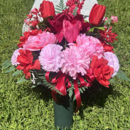 Pink and red floral arrangement in a green vase with a ribbon bow