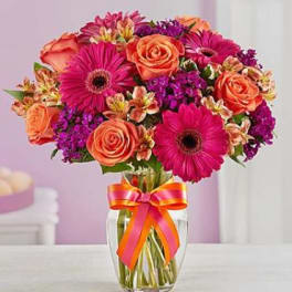 Bouquet of orange roses and pink gerbera daisies in a glass vase with a ribbon