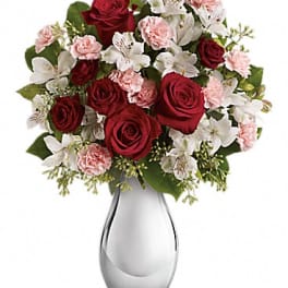 Bouquet of red roses, pink carnations, and white lilies in a glass vase
