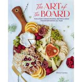 A charcuterie board with fruit, cheese, crackers, and flowers on a book cover