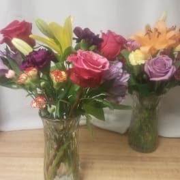 Two mixed flower bouquets in clear glass vases with roses and lilies