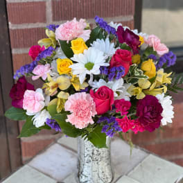 Mixed bouquet of roses, daisies, carnations, and orchids in a white vase