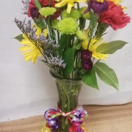Mixed bouquet of yellow, red, and purple flowers in a clear glass vase