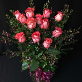Pink roses arranged in a clear glass vase with a purple ribbon