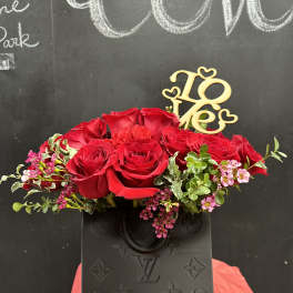 Red roses arranged in a black vase with a gold "Love" topper.