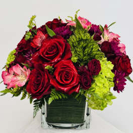 Bouquet of red roses, pink alstroemeria, and purple blooms in a square glass vase