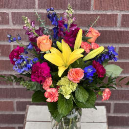 Colorful mixed bouquet with yellow lilies, roses, and carnations in a glass vase