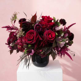 Deep red rose arrangement in a black vase on a white pedestal