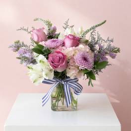 Pink and white mixed bouquet in a glass vase with a striped ribbon